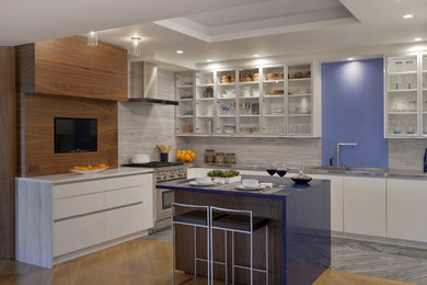 Mid-sized trendy u-shaped porcelain tile eat-in kitchen photo in New York with an undermount sink, flat-panel cabinets, white cabinets, stainless steel countertops, multicolored backsplash, glass sheet backsplash, paneled appliances and an island