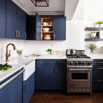 Small trendy dark wood floor and brown floor kitchen photo in New York with a farmhouse sink, blue cabinets, white backsplash, stainless steel appliances, white countertops, flat-panel cabinets, quartzite countertops, subway tile backsplash and no island