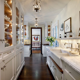Traditional kitchen pantry designs - Example of a classic galley brown floor and dark wood floor kitchen pantry design in Chicago with recessed-panel cabinets, white cabinets, marble countertops, white backsplash, marble backsplash, an island, white countertops and a farmhouse sink