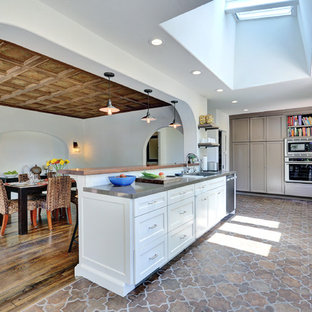 This is an example of a large mediterranean l-shaped eat-in kitchen in Los Angeles with shaker cabinets, white cabinets, stainless steel appliances, solid surface benchtops, with island, an undermount sink, beige splashback, brick splashback, terra-cotta floors and multi-coloured floor.