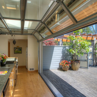 Design ideas for a mid-sized beach style single-wall kitchen in Seattle with a drop-in sink, flat-panel cabinets, brown cabinets, granite benchtops, green splashback, stone slab splashback, stainless steel appliances, light hardwood floors, no island and green benchtop.