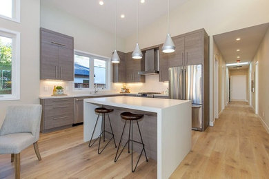 Inspiration for a mid-sized transitional l-shaped light wood floor and beige floor open concept kitchen remodel in San Francisco with an undermount sink, flat-panel cabinets, gray cabinets, solid surface countertops, stainless steel appliances, an island and white countertops
