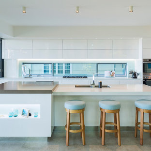 Photo of an expansive contemporary kitchen in Cairns with white cabinets, solid surface benchtops, stainless steel appliances, porcelain floors, with island, grey floor, white benchtop, an undermount sink, flat-panel cabinets and window splashback.