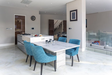 This is an example of a large contemporary grey and cream galley open plan kitchen in Other with flat-panel cabinets, an island, white cabinets, quartz worktops, white worktops, a single-bowl sink, black appliances, porcelain flooring and white floors.