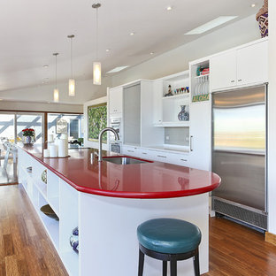 Inspiration pour une cuisine linéaire design fermée et de taille moyenne avec un évier encastré, un placard à porte plane, des portes de placard blanches, un électroménager en acier inoxydable, un sol en bois foncé, un îlot central, un plan de travail en quartz modifié, un sol marron et un plan de travail rouge.