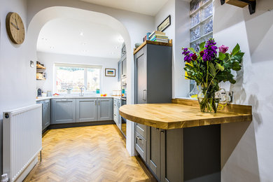 This is an example of a medium sized contemporary u-shaped enclosed kitchen in Other with a single-bowl sink, shaker cabinets, grey cabinets, laminate countertops, white splashback, glass sheet splashback, integrated appliances, vinyl flooring, a breakfast bar, brown floors and white worktops.
