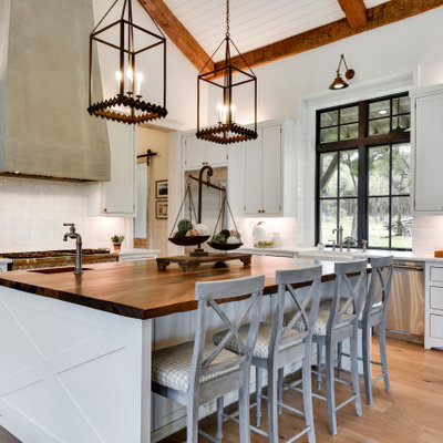 Open concept kitchen - large farmhouse l-shaped light wood floor and beige floor open concept kitchen idea in Austin with a farmhouse sink, shaker cabinets, white cabinets, white backsplash, stainless steel appliances, an island and white countertops