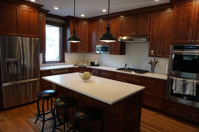 Enclosed kitchen - mid-sized transitional u-shaped medium tone wood floor and brown floor enclosed kitchen idea in Chicago with a drop-in sink, recessed-panel cabinets, dark wood cabinets, quartz countertops, white backsplash, subway tile backsplash, stainless steel appliances and an island