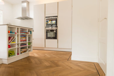 Example of a mid-sized classic galley light wood floor kitchen design in Toronto with an integrated sink, flat-panel cabinets, white cabinets, concrete countertops, white backsplash, stone slab backsplash, white appliances and an island