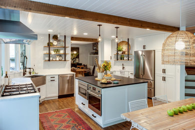 Eat-in kitchen - farmhouse u-shaped medium tone wood floor, brown floor, exposed beam and shiplap ceiling eat-in kitchen idea in Portland with a farmhouse sink, shaker cabinets, white cabinets, white backsplash, stainless steel appliances, an island and black countertops