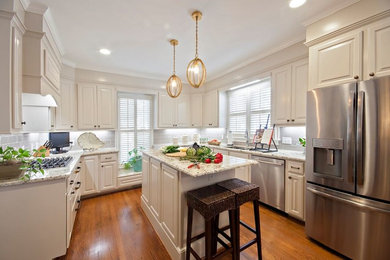Example of a mid-sized classic u-shaped medium tone wood floor and brown floor eat-in kitchen design in Other with an undermount sink, raised-panel cabinets, white cabinets, granite countertops, gray backsplash, subway tile backsplash, stainless steel appliances and an island