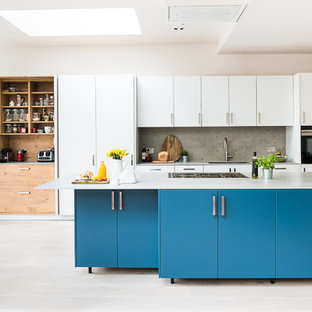 Photo of a large contemporary galley open plan kitchen in London with an integrated sink, flat-panel cabinets, turquoise cabinets, concrete benchtops, grey splashback, slate splashback, stainless steel appliances, light hardwood floors, with island, grey floor and grey benchtop.