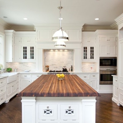 Enclosed kitchen - mid-sized traditional l-shaped dark wood floor enclosed kitchen idea in Chicago with recessed-panel cabinets, a farmhouse sink, wood countertops, white cabinets, white backsplash, stone tile backsplash, stainless steel appliances and an island