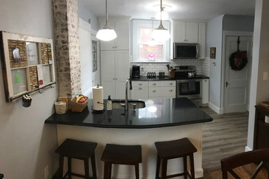 Example of a small farmhouse galley medium tone wood floor and brown floor eat-in kitchen design in Other with an undermount sink, shaker cabinets, white cabinets, solid surface countertops, white backsplash, subway tile backsplash, stainless steel appliances and a peninsula