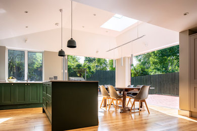Medium sized contemporary l-shaped kitchen/diner in London with shaker cabinets, green cabinets, engineered stone countertops, stainless steel appliances, medium hardwood flooring, an island, white worktops and a vaulted ceiling.