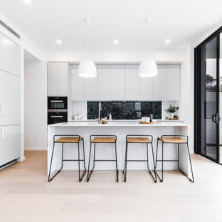 Design ideas for a mid-sized modern l-shaped kitchen in Sydney with flat-panel cabinets, grey cabinets, window splashback, black appliances, light hardwood floors, with island, beige floor and white benchtop.