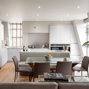 Photo of a medium sized contemporary grey and white l-shaped kitchen/diner in London with a built-in sink, grey cabinets, composite countertops, white splashback, ceramic splashback, stainless steel appliances, light hardwood flooring, an island, grey floors and white worktops.