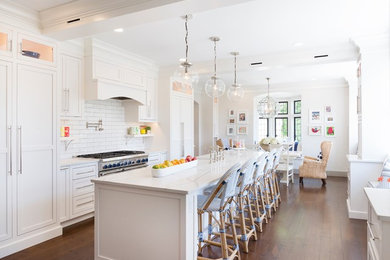 Foto de cocina comedor alargada costera con armarios estilo shaker, puertas de armario blancas, salpicadero blanco, electrodomésticos de acero inoxidable, suelo de madera en tonos medios y una isla