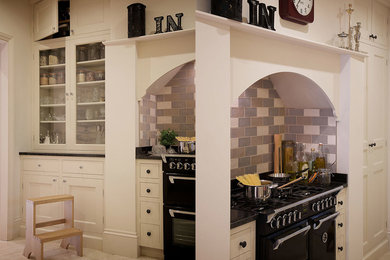 Moderne Küche mit Schrankfronten im Shaker-Stil, beigen Schränken, schwarzen Elektrogeräten, Kücheninsel und schwarzer Arbeitsplatte in Cheshire