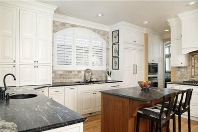 Large transitional light wood floor open concept kitchen photo in Denver with an undermount sink, raised-panel cabinets, white cabinets, granite countertops, black backsplash, subway tile backsplash, paneled appliances and two islands