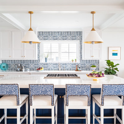 Example of a mid-sized beach style l-shaped light wood floor and brown floor eat-in kitchen design in Philadelphia with shaker cabinets, blue backsplash, stainless steel appliances, an island, white countertops, a farmhouse sink, white cabinets, quartzite countertops and ceramic backsplash