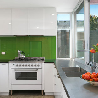 This is an example of a contemporary u-shaped eat-in kitchen in Other with a drop-in sink, white cabinets, green splashback, glass sheet splashback, no island, grey benchtop, flat-panel cabinets, zinc benchtops and stainless steel appliances.