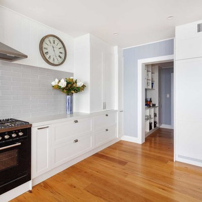 Example of a large classic u-shaped medium tone wood floor and brown floor open concept kitchen design in Sydney with an undermount sink, shaker cabinets, white cabinets, quartz countertops, gray backsplash, subway tile backsplash, black appliances and white countertops