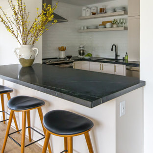 Inspiration for a small transitional u-shaped eat-in kitchen in Philadelphia with an undermount sink, shaker cabinets, beige cabinets, soapstone benchtops, white splashback, subway tile splashback, stainless steel appliances, vinyl floors, a peninsula, beige floor and black benchtop.