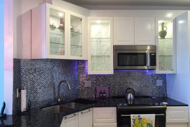 Inspiration for a large contemporary u-shaped porcelain tile kitchen remodel in Miami with an undermount sink, glass-front cabinets, white cabinets, granite countertops, metallic backsplash, glass tile backsplash and stainless steel appliances