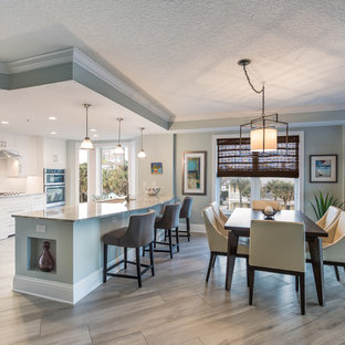 Photo of a beach style kitchen in Jacksonville with an undermount sink, ceramic floors, grey floor, shaker cabinets, white cabinets, granite benchtops, white splashback, limestone splashback, stainless steel appliances, with island and brown benchtop.