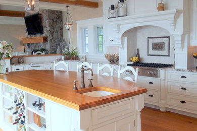 Example of a classic kitchen design in Portland Maine with wood countertops, white cabinets and stainless steel appliances