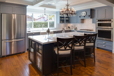 Mid-sized transitional l-shaped medium tone wood floor open concept kitchen photo in San Diego with a farmhouse sink, shaker cabinets, gray cabinets, quartz countertops, white backsplash, subway tile backsplash, stainless steel appliances and an island
