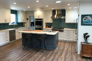 Inspiration for a mid-sized transitional u-shaped medium tone wood floor kitchen remodel in San Diego with an undermount sink, shaker cabinets, white cabinets, quartz countertops, blue backsplash, glass tile backsplash, stainless steel appliances, an island and white countertops
