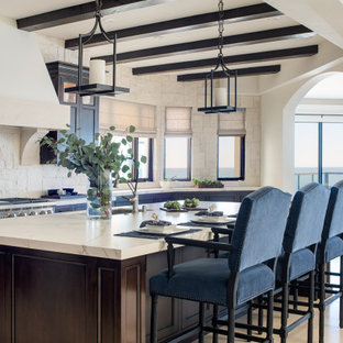 Diseño de cocina de galera, mediterránea, grande, abierta, con fregadero bajoencimera, armarios con paneles empotrados, puertas de armario de madera en tonos medios, encimera de acrílico, salpicadero beige, salpicadero de piedra caliza, electrodomésticos con paneles, suelo de piedra caliza, una isla, suelo beige y encimeras beige