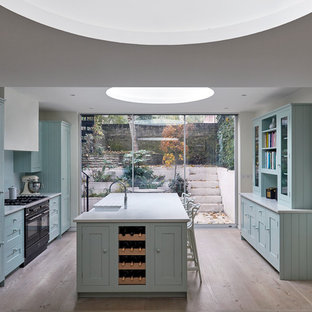 Ispirazione per una cucina chic di medie dimensioni con lavello stile country, ante blu, elettrodomestici neri, isola, ante in stile shaker e parquet chiaro