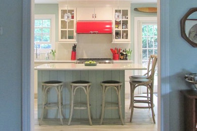 This is an example of an eclectic kitchen in New York with a double-bowl sink, flat-panel cabinets, white cabinets, engineered stone countertops, white splashback, metro tiled splashback, integrated appliances, porcelain flooring, an island, brown floors and white worktops.