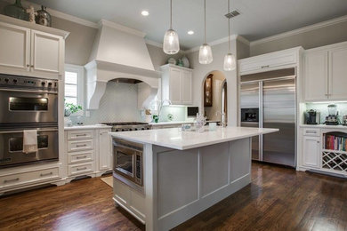 Inspiration for a mid-sized timeless l-shaped dark wood floor kitchen remodel in Dallas with a single-bowl sink, recessed-panel cabinets, white cabinets, quartzite countertops, green backsplash, glass tile backsplash, stainless steel appliances and an island