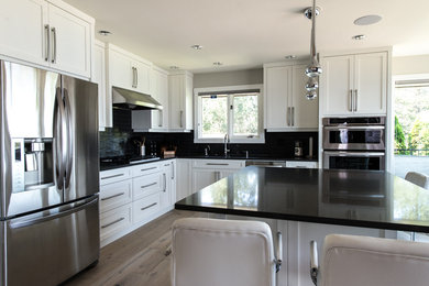 Photo of a medium sized contemporary l-shaped kitchen/diner in Vancouver with a submerged sink, shaker cabinets, white cabinets, engineered stone countertops, black splashback, glass tiled splashback, stainless steel appliances, light hardwood flooring and an island.