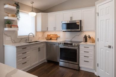 Mid-sized trendy u-shaped vinyl floor and brown floor enclosed kitchen photo in Calgary with an undermount sink, shaker cabinets, white cabinets, quartz countertops, white backsplash, marble backsplash, stainless steel appliances, an island and white countertops