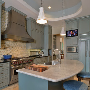 Large traditional kitchen inspiration - Example of a large classic l-shaped travertine floor kitchen design in Houston with a farmhouse sink, raised-panel cabinets, blue cabinets, granite countertops, multicolored backsplash, porcelain backsplash, paneled appliances and an island