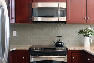 Small elegant u-shaped ceramic tile eat-in kitchen photo in Philadelphia with an undermount sink, recessed-panel cabinets, dark wood cabinets, granite countertops, green backsplash, glass tile backsplash and stainless steel appliances