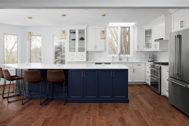 Inspiration for a transitional l-shaped medium tone wood floor and brown floor eat-in kitchen remodel in Toronto with an undermount sink, shaker cabinets, white cabinets, quartzite countertops, white backsplash, marble backsplash, stainless steel appliances, an island and white countertops