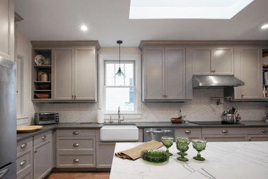 Example of a large transitional u-shaped medium tone wood floor eat-in kitchen design in DC Metro with a farmhouse sink, shaker cabinets, gray cabinets, gray backsplash, mosaic tile backsplash, stainless steel appliances and an island