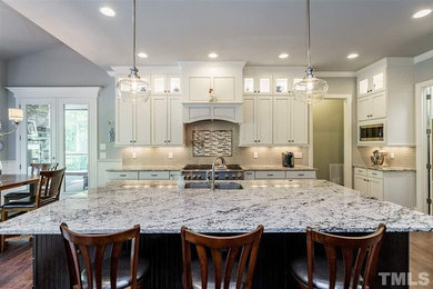 Inspiration for a large transitional l-shaped dark wood floor and brown floor eat-in kitchen remodel in Raleigh with an undermount sink, shaker cabinets, white cabinets, granite countertops, beige backsplash, glass tile backsplash, stainless steel appliances, an island and white countertops