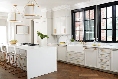 Example of a transitional dark wood floor and brown floor kitchen design in Other with a farmhouse sink, shaker cabinets, beige cabinets, white backsplash, an island and white countertops