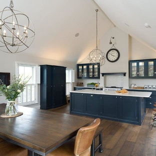 Photo of a large rustic single-wall kitchen/diner in Other with a belfast sink, glass-front cabinets, blue cabinets, quartz worktops, white splashback, metro tiled splashback, stainless steel appliances, dark hardwood flooring, an island, brown floors and white worktops.