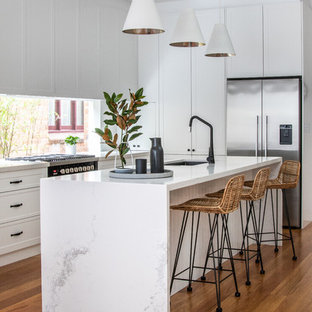 Inspiration for a contemporary l-shaped eat-in kitchen in Sydney with white cabinets, quartz benchtops, window splashback, an undermount sink, recessed-panel cabinets, stainless steel appliances, medium hardwood floors, with island, brown floor and white benchtop.