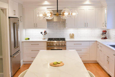 ボストンにある高級な広いトランジショナルスタイルのおしゃれなキッチン (アンダーカウンターシンク、シェーカースタイル扉のキャビネット、白いキャビネット、クオーツストーンカウンター、白いキッチンパネル、セラミックタイルのキッチンパネル、シルバーの調理設備、淡色無垢フローリング、茶色い床、白いキッチンカウンター) の写真