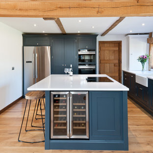 Medium sized farmhouse l-shaped enclosed kitchen in Kent with a belfast sink, blue cabinets, quartz worktops, stainless steel appliances, light hardwood flooring, an island, beige floors, white worktops and shaker cabinets.