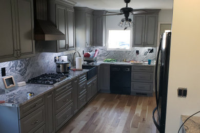 Example of a mid-sized country galley light wood floor eat-in kitchen design in Bridgeport with a farmhouse sink, raised-panel cabinets, distressed cabinets, granite countertops, gray backsplash, granite backsplash, black appliances, no island and gray countertops